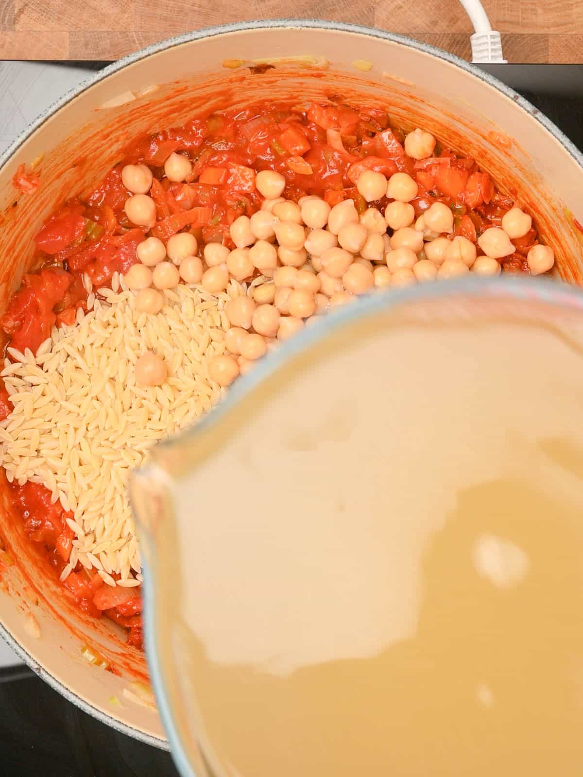 pouring stock to chickpea orzo soup